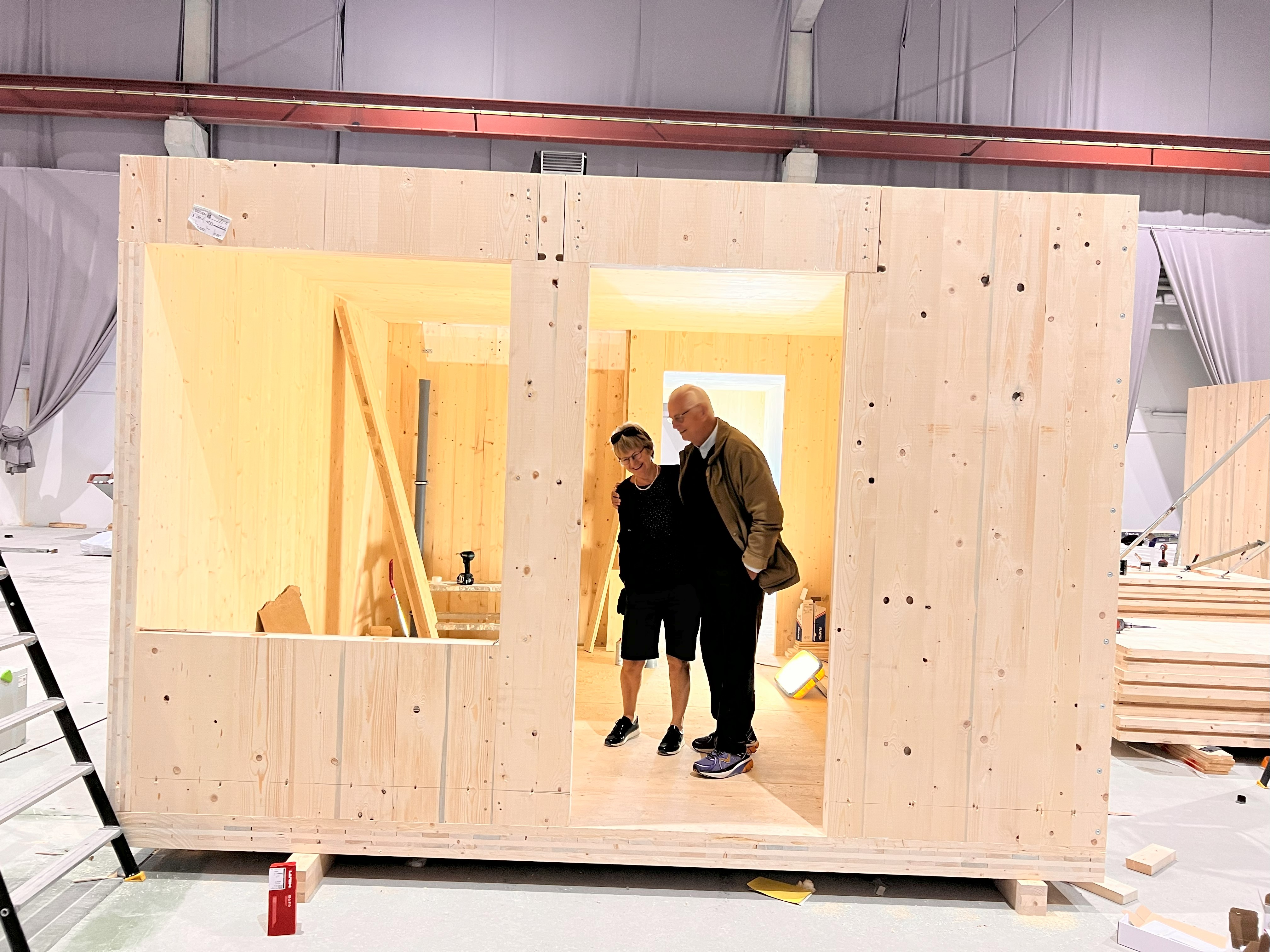 Två personer inspekterar en modern träbyggnad inomhus med träpaneler.